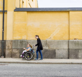 Assistant helping disabled woman in wheelchair move around city