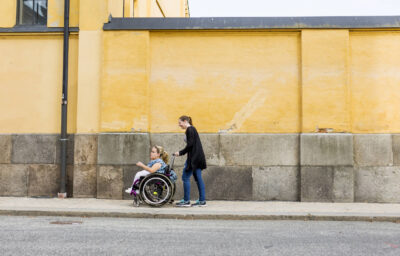 Assistant helping disabled woman in wheelchair move around city