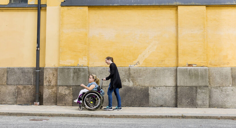 Assistant helping disabled woman in wheelchair move around city