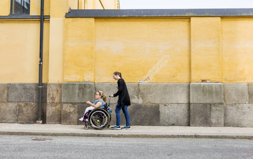 Assistant helping disabled woman in wheelchair move around city