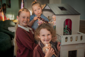 Three girl smiling while playing with a doll house at PCYC Tamworth Outside Of School Hours Care.