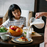 Crop woman pouring milk for little girl