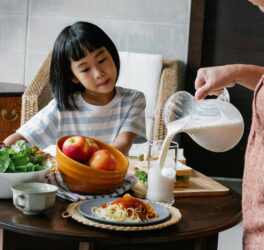 Crop woman pouring milk for little girl