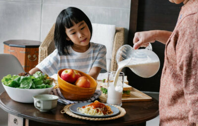 Crop woman pouring milk for little girl
