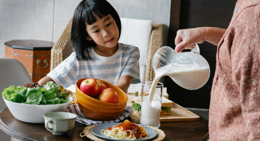 Crop woman pouring milk for little girl