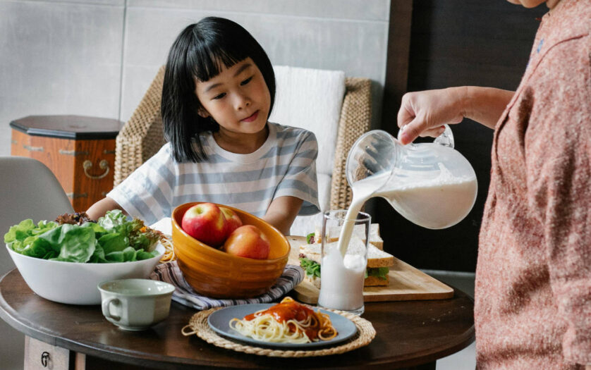 Crop woman pouring milk for little girl