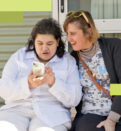 A young woman shows her friend what she's doing online as they sit together on a porch