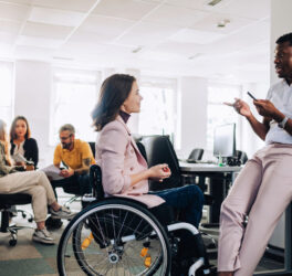 woman in wheelchair talking with her colleague in the office