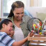 Cheerful young boy with Down Syndrome plays with a bead maze with a play therapist.