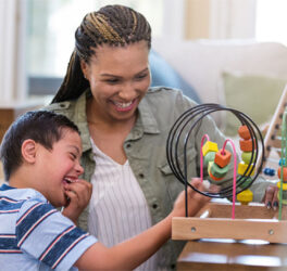 Cheerful young boy with Down Syndrome plays with a bead maze with a play therapist.