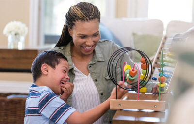 Cheerful young boy with Down Syndrome plays with a bead maze with a play therapist.