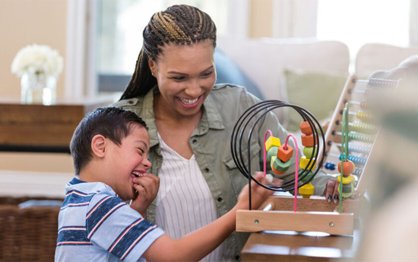 Cheerful young boy with Down Syndrome plays with a bead maze with a play therapist.