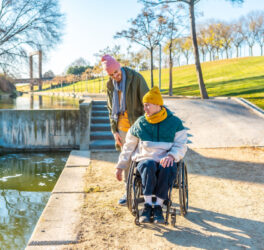 Men in wheelchair with his friend spending time together in the park during a sunny day