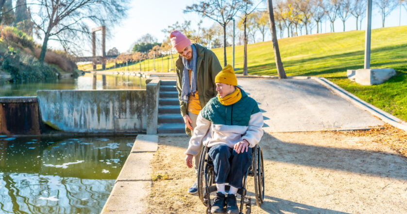 Men in wheelchair with his friend spending time together in the park during a sunny day