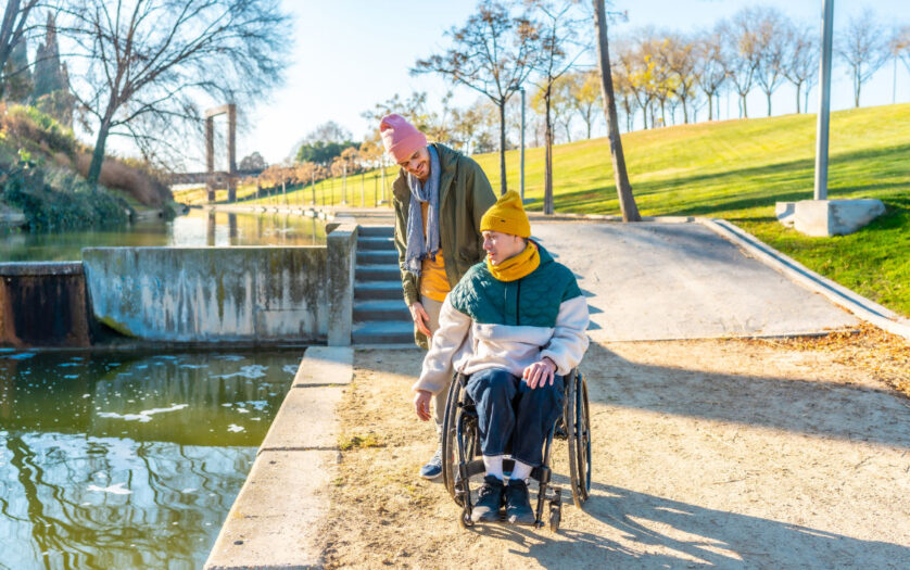 Men in wheelchair with his friend spending time together in the park during a sunny day