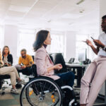 Women in wheelchair talking with her colleage in the office