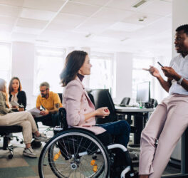 Women in wheelchair talking with her colleage in the office