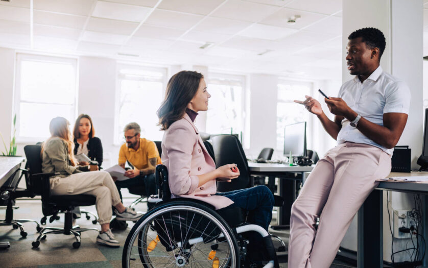 Women in wheelchair talking with her colleage in the office