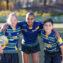 Three children wearing rugby uniforms in a huddle on a playing field facing towards the camera.