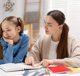 Mother and her upset daughter reading book at table indoors