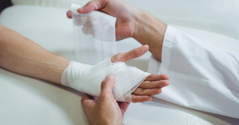 Doctor putting bandage on injured hand of patient in clinic