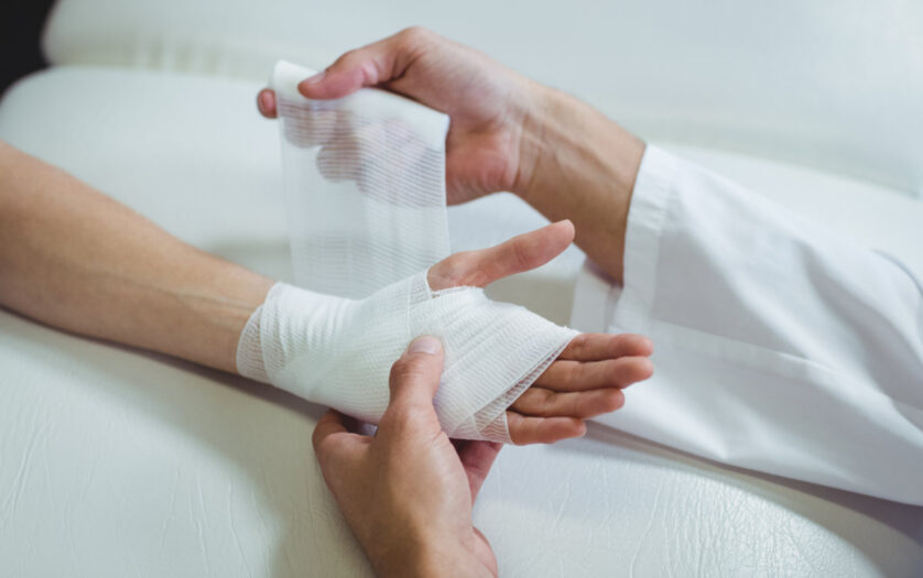 Doctor putting bandage on injured hand of patient in clinic
