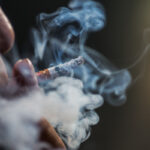 Closeup shot of a person puffing on a cigarette surrounded with smoke