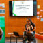 Ms Ogolo-Dickson presenting at an indoor event, with a presentation screen behind them and a lectern and laptop nearby.