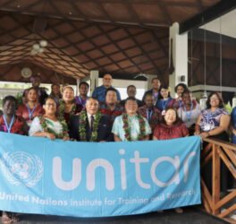 A group of participants from the Pacific stand in front of a UNITAR banner for a group photo