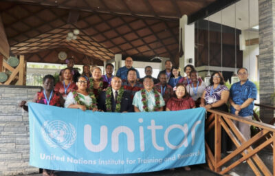 A group of participants from the Pacific stand in front of a UNITAR banner for a group photo