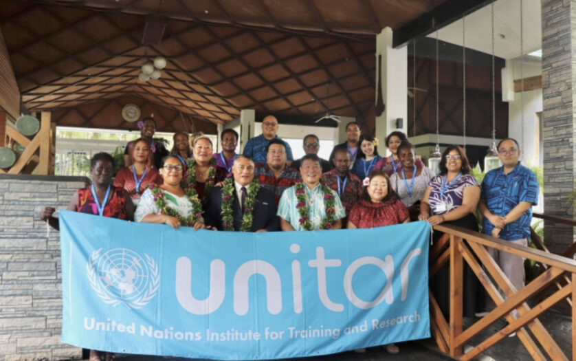 A group of participants from the Pacific stand in front of a UNITAR banner for a group photo