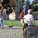 A Man in wheelchair outdoors in Rome. On the background the Arch of Constantine and the horse.