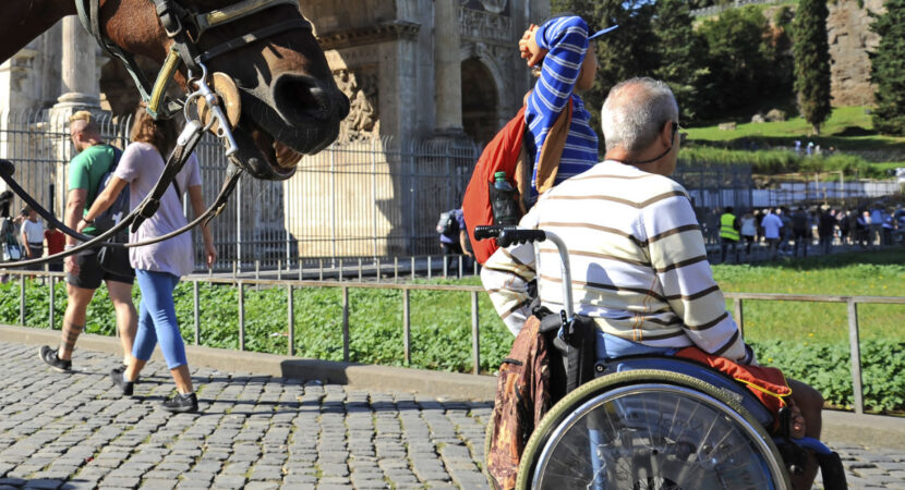 A Man in wheelchair outdoors in Rome. On the background the Arch of Constantine and the horse.