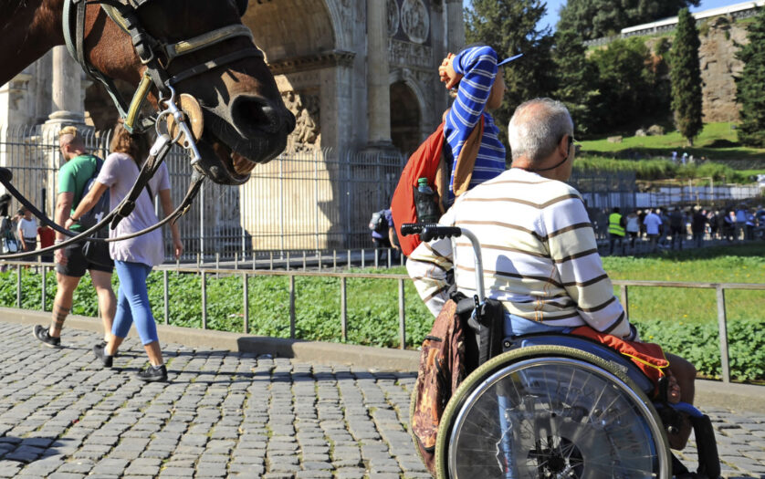 A Man in wheelchair outdoors in Rome. On the background the Arch of Constantine and the horse.