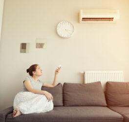 Woman turns on the air conditioner from the remote control sitting on the sofa.