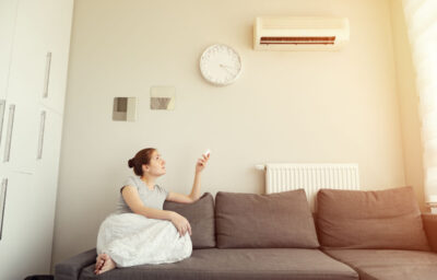 Woman turns on the air conditioner from the remote control sitting on the sofa.
