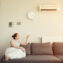 Woman turns on the air conditioner from the remote control sitting on the sofa.