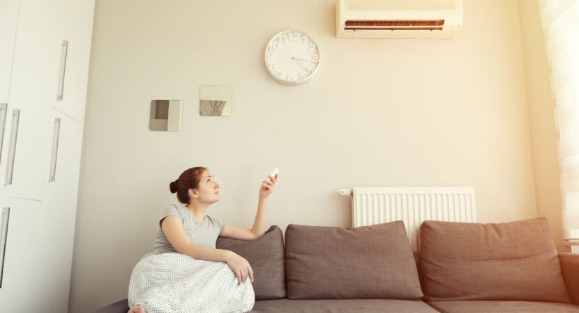Woman turns on the air conditioner from the remote control sitting on the sofa.