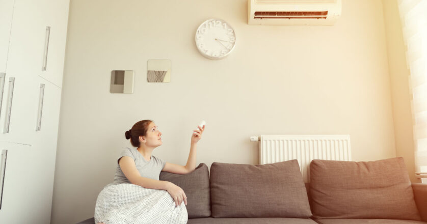 Woman turns on the air conditioner from the remote control sitting on the sofa.