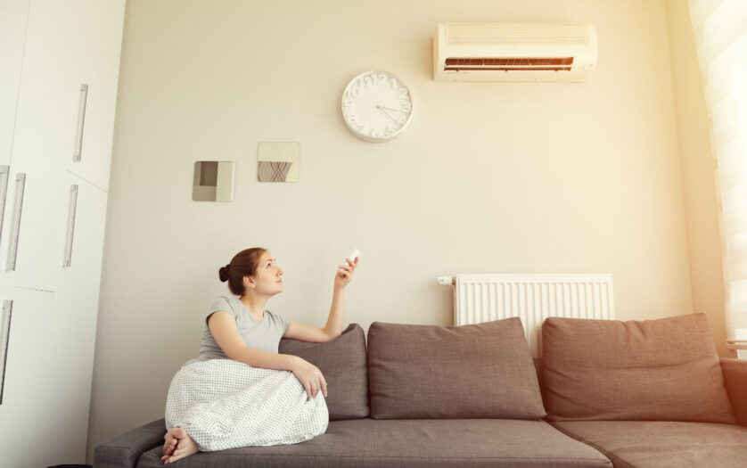 Woman turns on the air conditioner from the remote control sitting on the sofa.