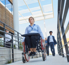 Business woman in a wheelchair in front of the office on a ramp with other workers