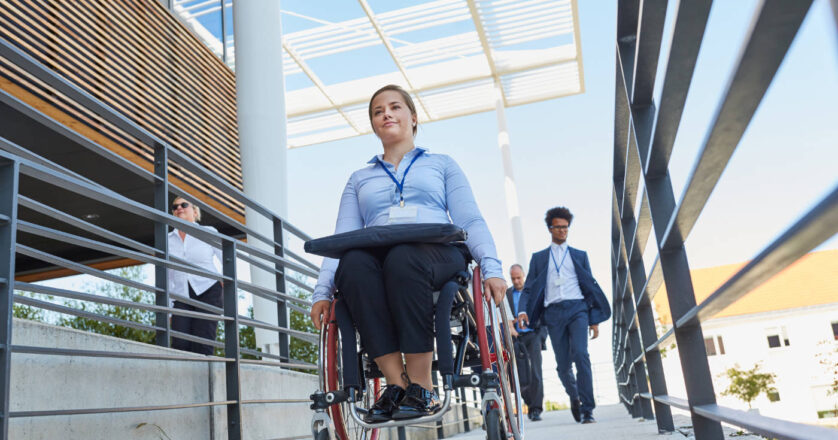 Business woman in a wheelchair in front of the office on a ramp with other workers