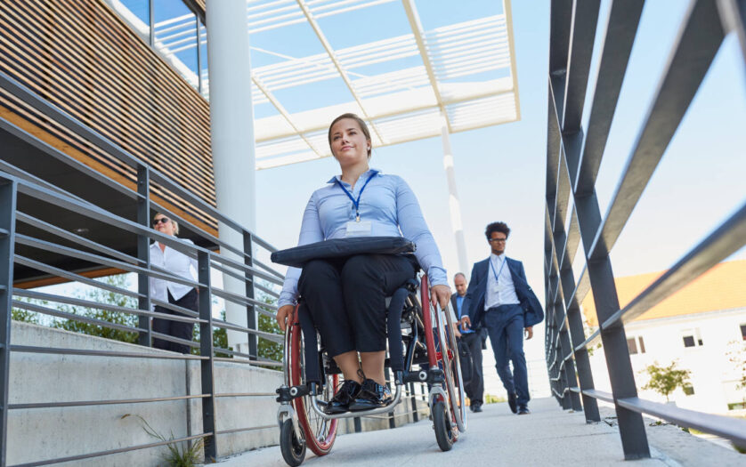 Business woman in a wheelchair in front of the office on a ramp with other workers