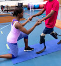 Side view of female physiotherapist helping disabled man walk with prosthetic leg in sports center.