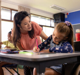 Diverse female teacher and schoolgirl in wheelchair in elementary school class.