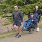 two peoTwo people help push an all-terrain wheelchair across rough terrain