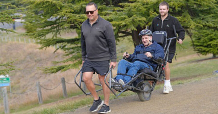 two peoTwo people help push an all-terrain wheelchair across rough terrain