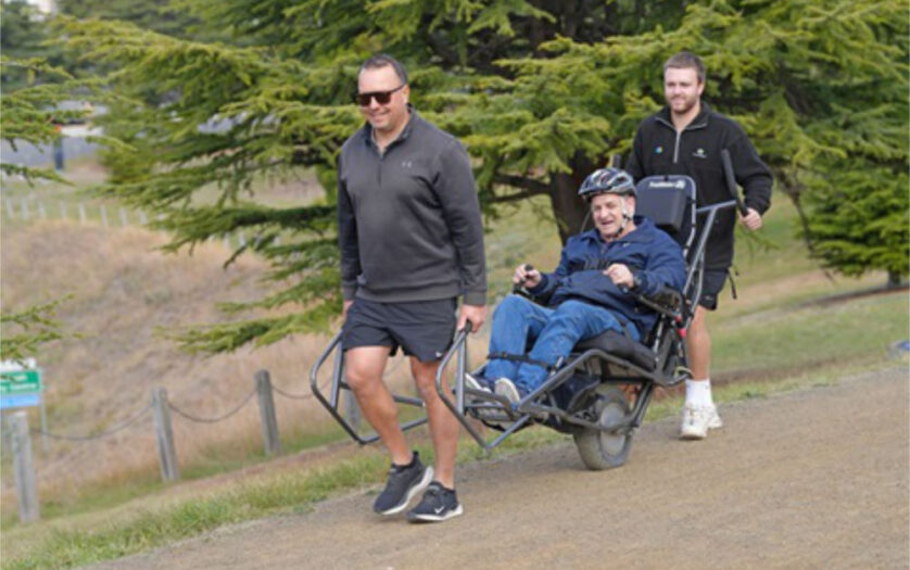 two peoTwo people help push an all-terrain wheelchair across rough terrain
