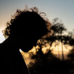 Silhouette of young man with fluffy hair formed by the backlit sun at dusk