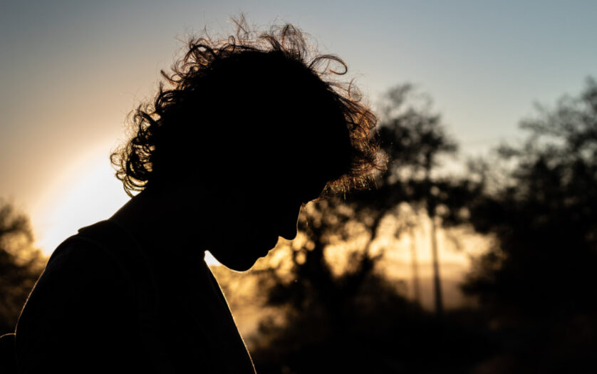 Silhouette of young man with fluffy hair formed by the backlit sun at dusk